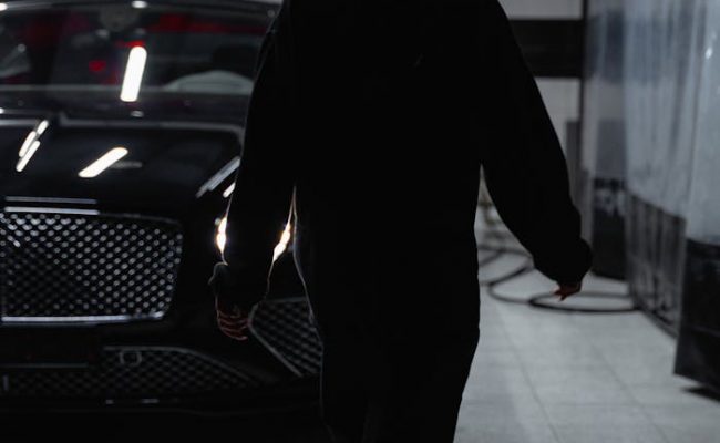Silhouette of a person walking towards a black car in a dimly lit garage.